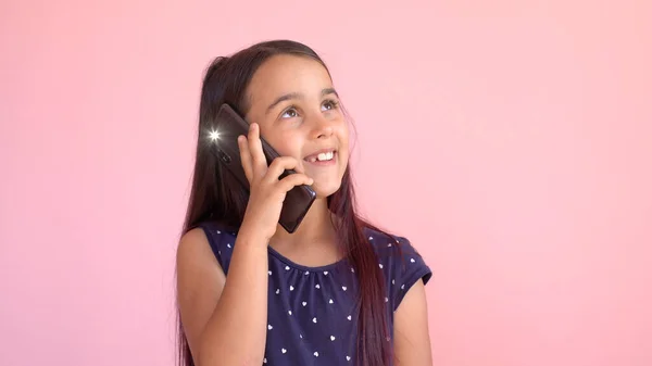 Pequeña niña en edad preescolar en un vestido con un teléfono móvil, aislado sobre rosa — Foto de Stock