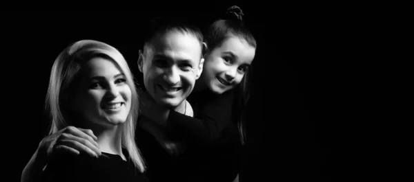 Joyful family mother, father and little girl in black clothes with dark background. Family portrait — Stock Photo, Image
