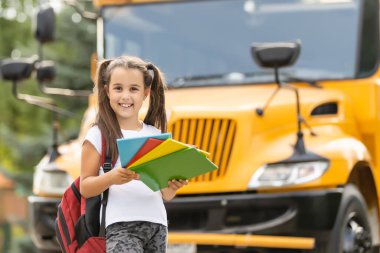 Otobüsün yanında duran sevimli kız okula gidiyor. Kameraya yakın çekim pozu veriyor.