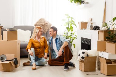 Yerde oturan gülümseyen çift kameradan başka tarafa bakıyor.