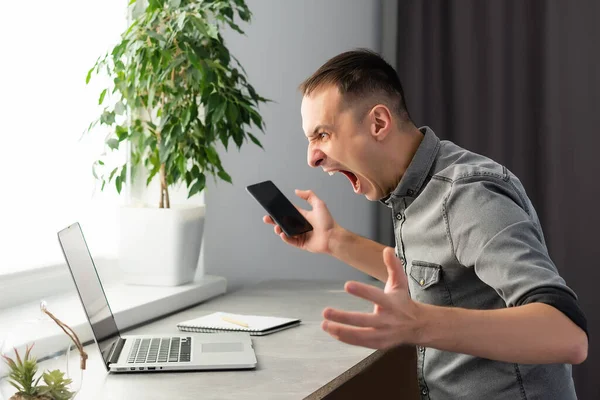 Jonge geschokte man gekleed in shirt tijdens het gebruik van laptop. op grijs. — Stockfoto