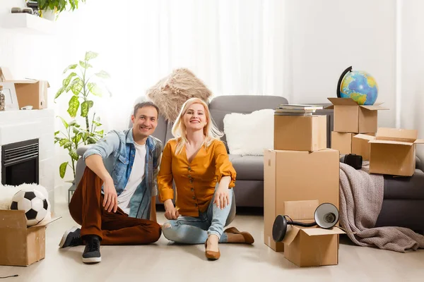 Piękna para siedzi między wieloma pudełkami w swoim nowym domu — Zdjęcie stockowe