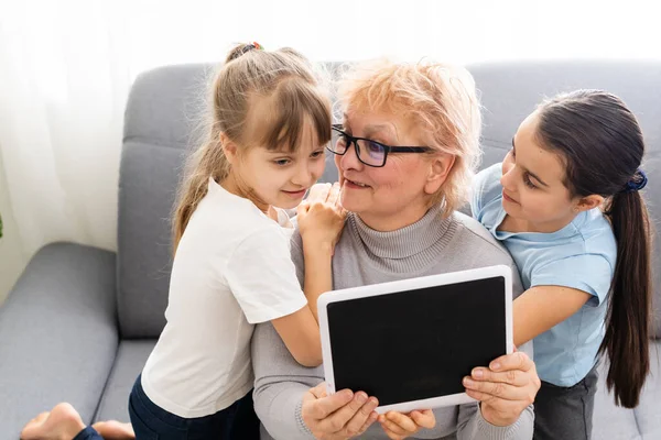 Nonna e due nipoti usano un tablet a casa — Foto Stock