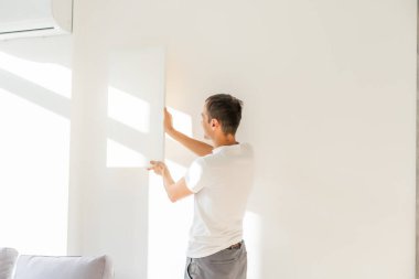 Beyaz tişörtlü genç adam boş tuval tutuyor. Erkek öğrenci gülümsüyor. Reklam, selamlama ve davetiye şablonu. Duygusal Portre