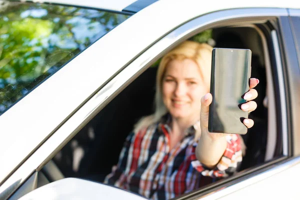 美丽的女人坐在车里，把她的智能手机展示在窗外 — 图库照片