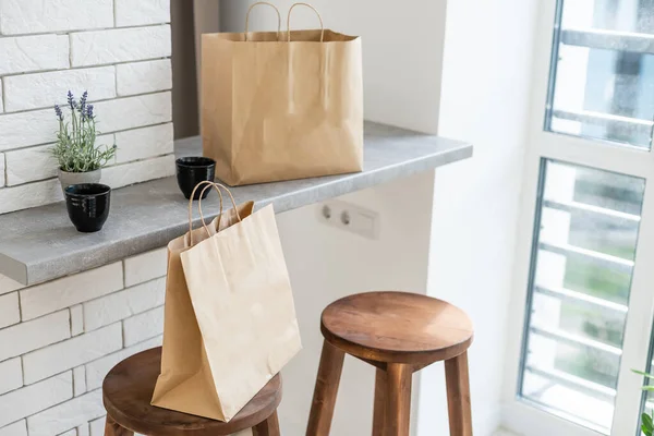 Mock-up of big brown paper package with handles, blank craft shopping bag with area for your logo or design, white wall in the background, food delivery concept