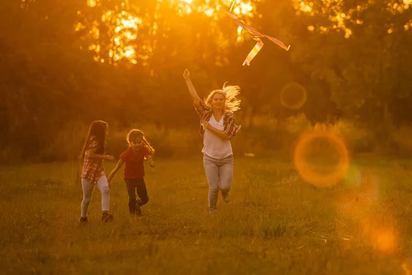 Glückliche Familienmutter und Kinder laufen im Sommer mit dem Drachen auf der Wiese in der Natur — Stockfoto