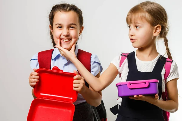 Alunos da escola primária com lancheiras nas mãos. Meninas com mochilas estão comendo frutas. Início das lições. Primeiro dia de queda. — Fotografia de Stock