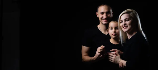 Gioiosa madre di famiglia, padre e bambina in abiti neri con sfondo scuro. Ritratto di famiglia — Foto Stock