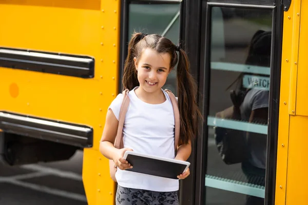 Χαριτωμένο κορίτσι με ένα σακίδιο στέκεται κοντά στο λεωφορείο πηγαίνει στο σχολείο ποζάροντας στην κάμερα σκεπτική γκρο πλαν — Φωτογραφία Αρχείου