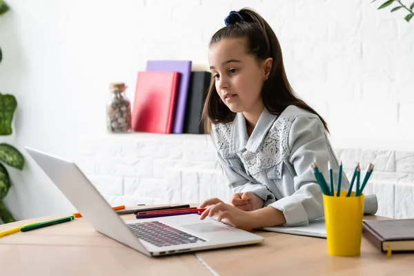 Klein meisje doet haar huiswerk thuis en met behulp van een laptop — Stockfoto