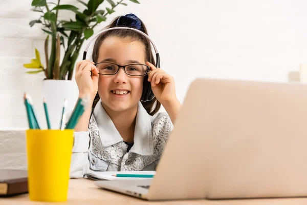 Het gelukkige meisje in hoofdtelefoon met een laptop aan tafel — Stockfoto