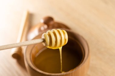 Koyu ahşap bir kasede bal, kırsal ahşap bir tabak. Tahta kaşık yavaşça damlıyor..