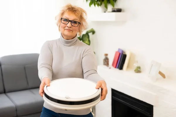 Oudere vrouw maakt gebruik van een robot stofzuiger thuis — Stockfoto