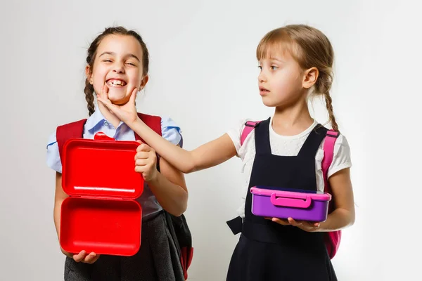 Alunos da escola primária com lancheiras nas mãos. Meninas com mochilas estão comendo frutas. Início das lições. Primeiro dia de queda. — Fotografia de Stock