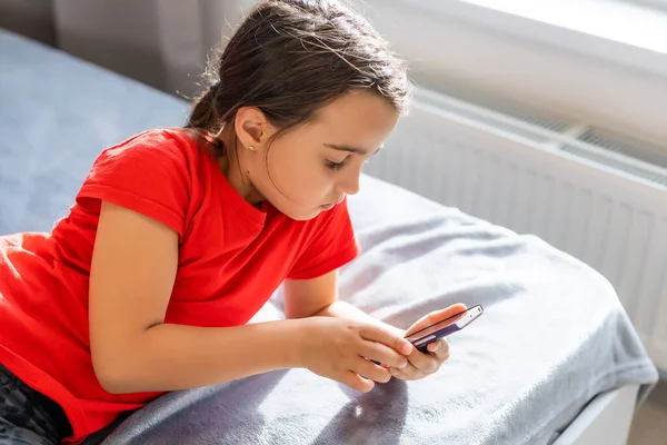 education, school, technology and internet concept - little student girl with smartphone at home