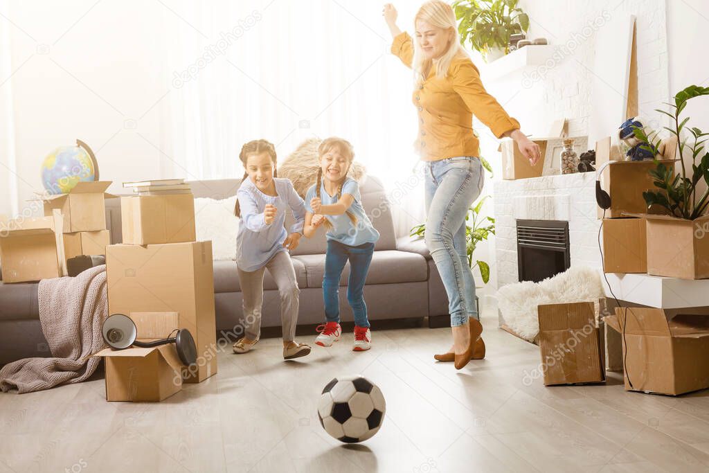 Pretty young mother and her cute little daughter having fun in new apartment and unpacking moving boxes