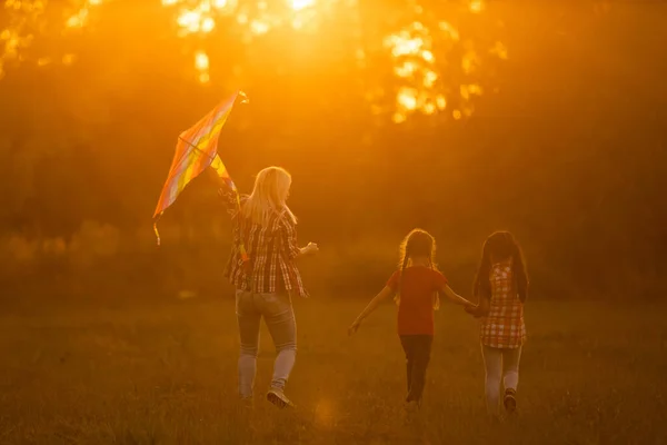 Glückliche Familienmutter und Kinder laufen im Sommer mit dem Drachen auf der Wiese in der Natur — Stockfoto