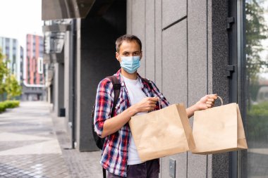 Paket teslimatçısı elinde yiyecek, koruyucu maskeli bir teslimatçı.