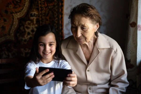 Бабуся і онучка. Мила дівчинка показує бабусі смартфон.. — стокове фото