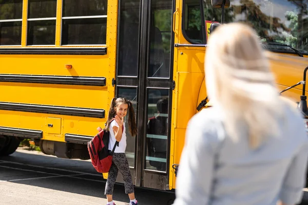 Niños estudiante corriendo en las manos de las madres para abrazarla después de regresar a la escuela cerca del autobús escolar — Foto de Stock