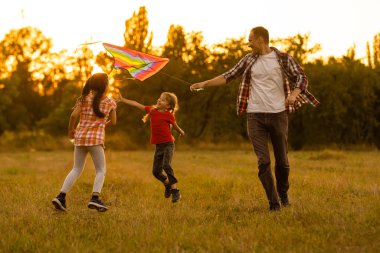 Mutlu aile babası ve kızı çayır üzerinde bir uçurtmayla koşuyor