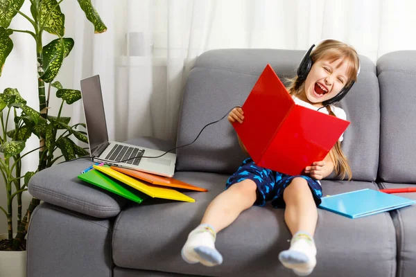 Foto de la pequeña alumna bonita escuela dama encienda el portátil skype lección en línea mantenga libro abierto respuesta lista profesor preguntas sentarse sofá distancia cuarentena estudio comodidad habitación interior — Foto de Stock