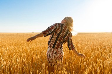 Batan güneşin arka planındaki buğday tarlasında bir kadın.