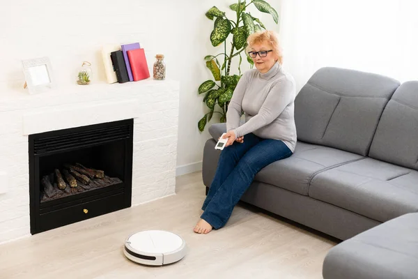 Människor, fritid, hushåll och teknik koncept - äldre kvinna, robot dammsugare golv i hemmet — Stockfoto