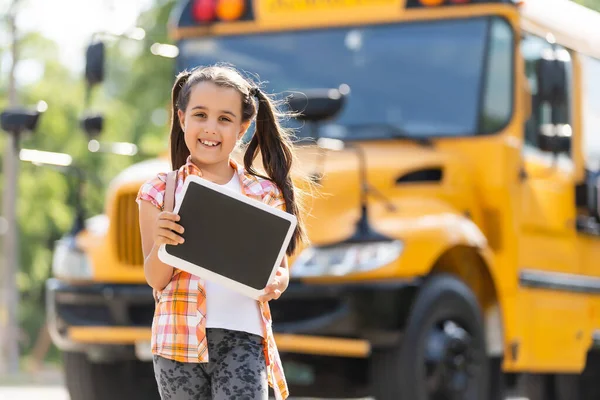 Κοριτσάκι στέκεται δίπλα σε μια μεγάλη πόρτα σχολικού λεωφορείου με το σακίδιό της. — Φωτογραφία Αρχείου