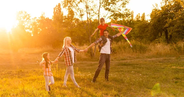 Szczęśliwa rodzina z latawcem grającym o zachodzie słońca na polu — Zdjęcie stockowe