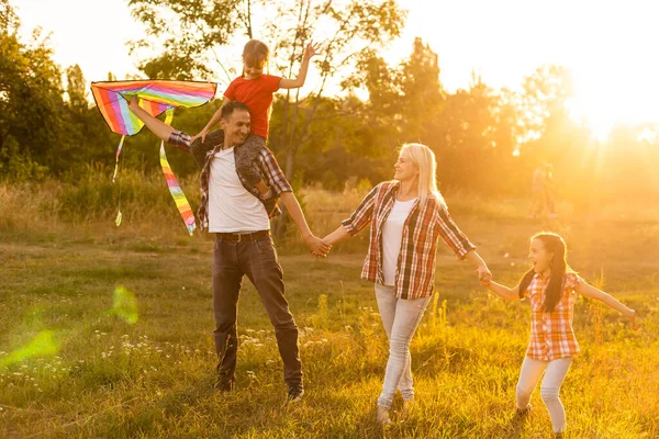 Pai de família feliz de mãe e filhas lançam um papagaio na natureza ao pôr do sol — Fotografia de Stock