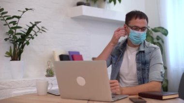 Adam koruyucu maskeyi çıkarmaya ve dizüstü bilgisayarla çalışmaya çalışıyor.