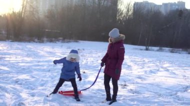 Aile, kızak, sezon ve insanlar konsepti - mutlu anne kışın dışarıda çocukla birlikte buz kızağı çekiyor