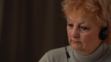 Kulaklık takan kıdemli bayan öğretmen bilgisayardan online ders veriyor.