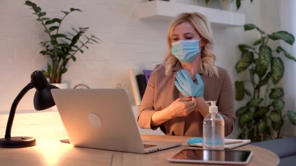 Ellerine eldiven takmış, maske takmış genç bir kadın evde ya da iş yerinde çalışırken salgın karantina sırasında virüsün yayılmasını önlüyor. — Stok video