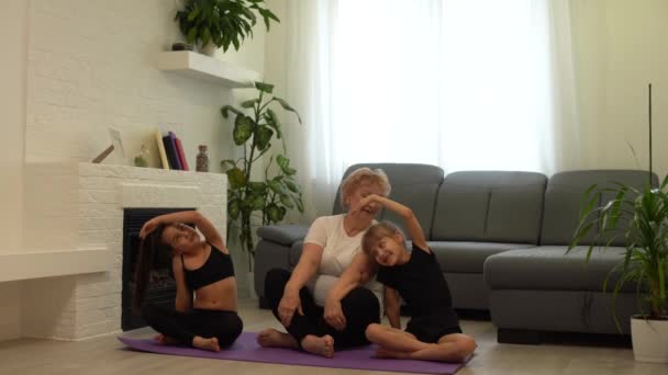 Vuxen kvinna med sina barnbarn. Morgonövningar, yoga - gör allt hemma tillsammans. Mormor — Stockvideo