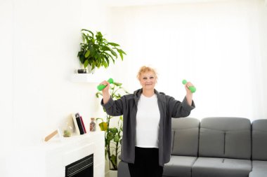 Evde halter egzersizi yapan, gülümseyen aktif son sınıf kadınının yakın plan portresi..