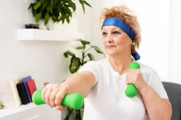 Close-up portret van actieve oudere vrouw doet halter oefeningen thuis, glimlachen. — Stockfoto