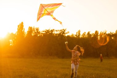 İki çocuk gün batımında parkta uçurtma uçuruyor.