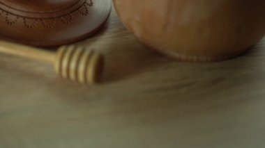 Koyu ahşap bir kasede bal, kırsal ahşap bir tabak. Tahta kaşık yavaşça damlıyor..