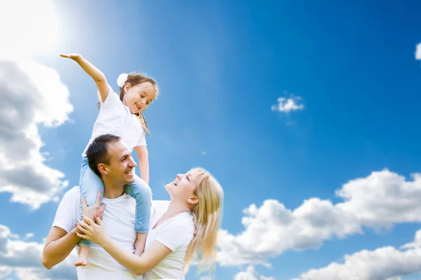Jeune famille heureuse s'amuser à l'extérieur, vêtue de blanc et avec le ciel bleu en arrière-plan — Photo