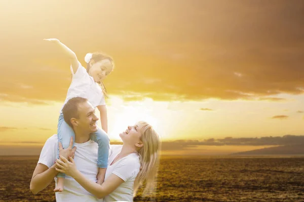 Jeune famille heureuse s'amuser à l'extérieur, vêtue de blanc et sur le ciel et le coucher du soleil — Photo