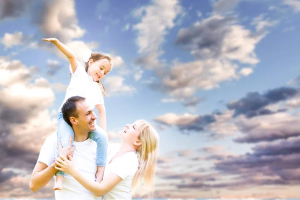 Fiatal boldog család szórakozás szabadban, öltözött fehér és kék ég a háttérben — Stock Fotó