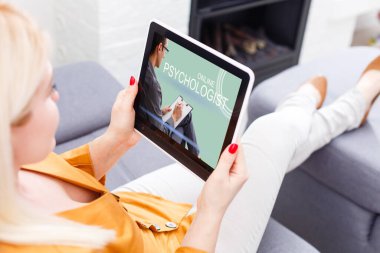 Tıbbi maskeli genç bir kadın ev karantinası sırasında çevrimiçi bir psikoloğu arıyor. Dijital tabletteki doktora video çağrısı.