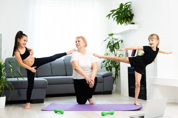 Senior grandmother workout yoga withgranddaughters preschooler. They are sitting on mat at cozy home interior. Sport, parenthood and people concept — Stock Photo, Image