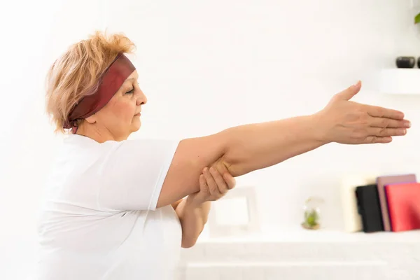 Ochtendtraining. Positieve senior dame die thuis haar handen opwarmt, lege ruimte — Stockfoto