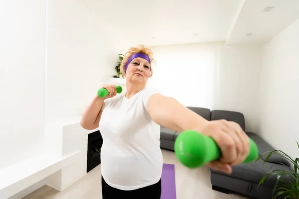 Tělocvična doma. Pozitivní starý žena školení s činkami v obývacím pokoji, kopírovat prostor — Stock fotografie