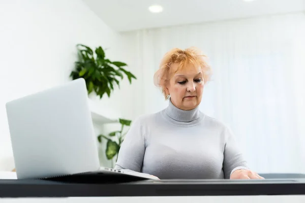 A nő szintetizátorozik, és nézi a laptop képernyőjét. Női kezek közelsége az elektromos zongorán. — Stock Fotó