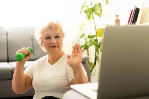 Domácí výcvik. Aktivní starší žena dělat cvičení v přední části notebooku doma, volné místo — Stock fotografie